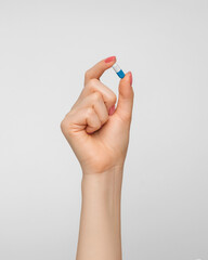 Pill in a capsule in a woman's hand with nude nail polish.