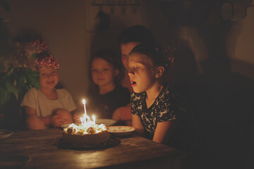 Cute child girl at table with birthday cake with siblings, dark style. Cake and candle 9 years...