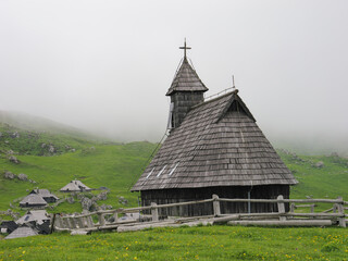 Fototapeta na wymiar Back view of a Church of the Mary of the Snows on a misty day, Velika Planina, Slovenia