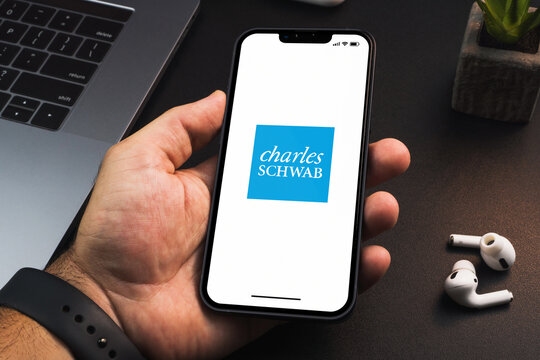 Man holding a smartphone with Charles Schwab financial app on the screen on black background table. Office environment. Rio de Janeiro, RJ, Brazil. June 2022