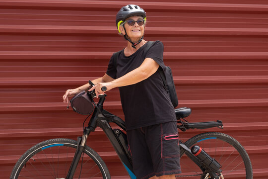Smiling senior cyclist woman in outdoor excursion in urban city with her electric bicycle. Healthy lifestyle for retired people and sustainable mobility concept