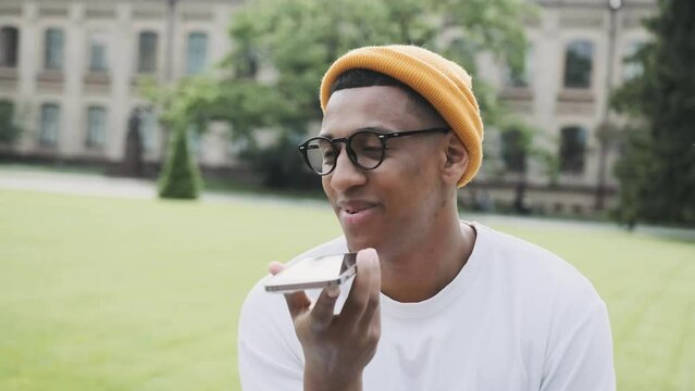 Happy young hipster is sitting in the park, talking onthe phone with a smile, Closeup portrait.