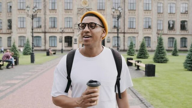 Motion scene of a young international student walks in the campus with a backpack and a coffee glass in his hand