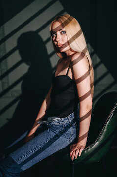 Girl sitting on chair in striped hard light, gobo mask. Studio portrait against green wall