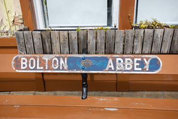Blue weathered Bolton Abbey sign on wooden bench Bolton Abbey railway station platform in Yorkshire, UK
