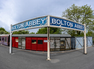 Blue weathered Bolton Abbey sign at platform in front of old train carriage at Bolton Abbey railway station, Yorkshire, UK