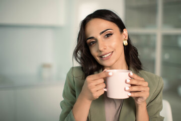 Smiling woman holding mug of coffee or tea, indoors at home in apartment, enjoying leisure time, morning or start of the day, relaxation and cozy, confident and independent