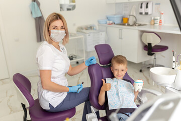 Dental clinic visit. Young positive woman dentist and small boy patient in dentist office