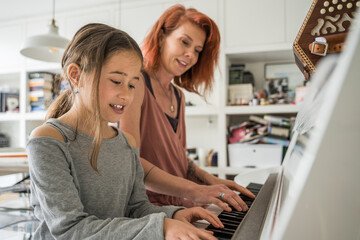 Ginger woman sitting at the piano and playing music together with her little daughter