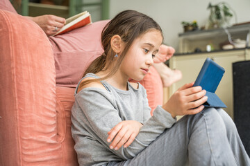 Obraz premium Caucasian girl sitting near the sofa and playing at the smartphone at home