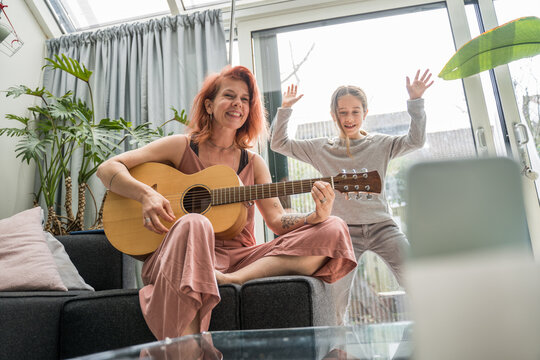 Ginger tattooed woman playing guitar while her child daughter dancing nearby