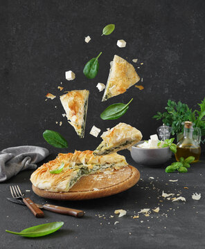 Traditional greek cuisine. Spanakopita pie and pieces with spinach and feta cheese on dark background.Lavitation food, dish with spinach