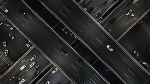 Top down drone aerial flying over modern multileveled intersection elevated paved asphalt road zoom out slow motion. Heavy traffic of vehicles night time lights, metropolis infrastructure development