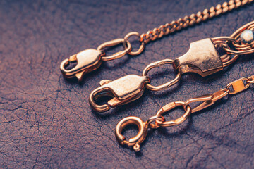Gold clasps of a golden chains lying on a leather background. Macro photography with soft focus. - obrazy, fototapety, plakaty