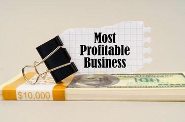 There are dollars on the table, on which there is a clip and torn paper with the inscription - Most Profitable Business © Dzmitry