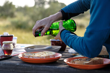 Crop person pouring oil on toast in countryside
