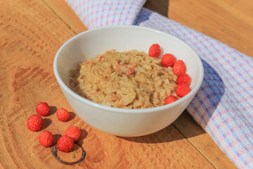 Oatmeal with wild strawberries in a plate on a wooden table. Red small berries are rich in vitamins. Healthy food for breakfast