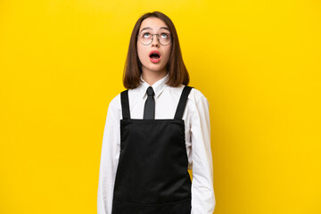 Young Ukrainian waitress woman isolated on yellow background looking up and with surprised...