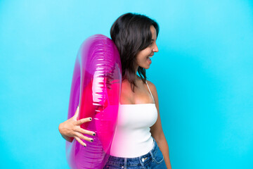 Young hispanic woman holding air mattress donut isolated on blue background laughing in lateral position