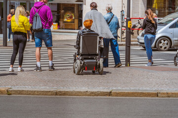 A disabled person in a wheelchair on a sunny day on a city street near a pedestrian crossing across...