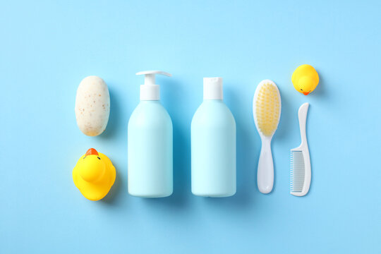 Baby Bathing Accessories On Blue Table Top View. Flat Lay Set Of Shampoo Bottles, Hair Comb, Body Brush, Soap, Yellow Ducks.