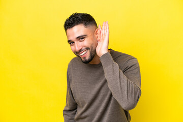 Young Arab handsome man isolated on yellow background listening to something by putting hand on the...