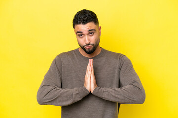 Young Arab handsome man isolated on yellow background keeps palm together. Person asks for something