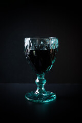 Green transparent wineglass with dark beverage on black background