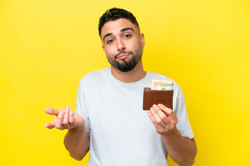 Young Arab man holding a wallet isolated on yellow background making doubts gesture while lifting the shoulders