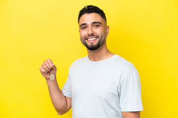 Young Arab man holding home keys isolated on yellow background smiling a lot