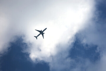Silhouette of airplane flying in sky with white clouds. Passenger plane at flight, travel concept