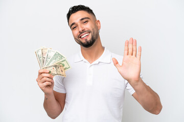 Young Arab man taking a lot of money isolated on white background saluting with hand with happy expression