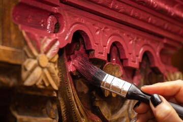 Closeup of brush in female hand painting detailed carved ornaments of old wooden sideboard buffet...