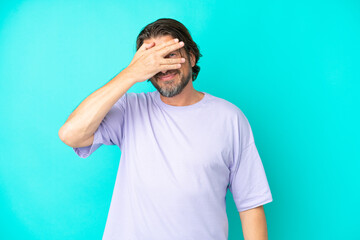 Senior dutch man isolated on blue background covering eyes by hands and smiling