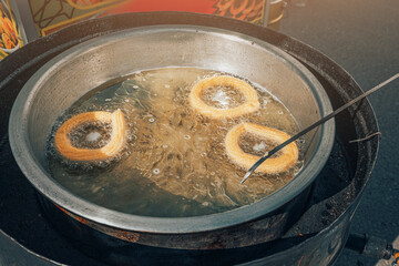 Spanish churros are boiled in boiling oil in a street food cafe. Unhealthy food that causes atherosclerosis and cholesterol plaques