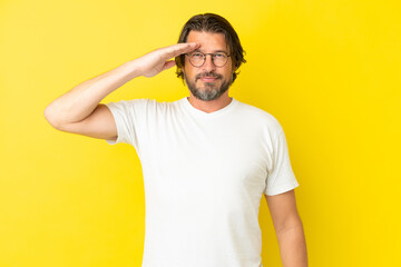 Senior dutch man isolated on yellow background saluting with hand with happy expression