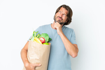 Senior dutch man holding grocery shopping bag over isolated background having doubts and thinking