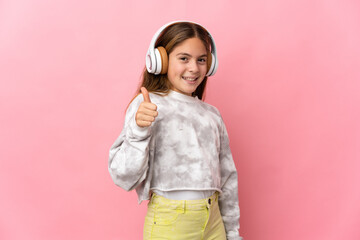 Child over isolated pink background listening music and with thumb up