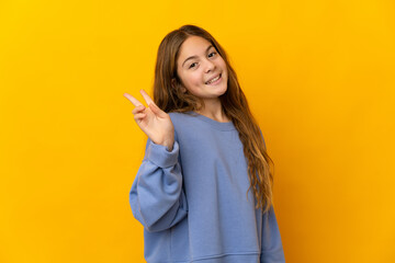 Child over isolated yellow background smiling and showing victory sign