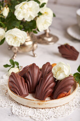 Madeleine cookies in a shape of seashells covered with dark chocolate. Traditional French Mini cakes with lemon flower. 