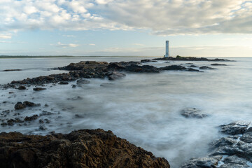 Sunrise with long exposure photograph of the beach with lighthouse on the horizon