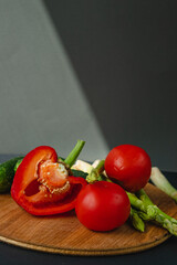branches of fresh green asparagus, peppers, tomatoes and cucumbers on a wooden board, dark gray background, top view. Basic trend concept with copy space.