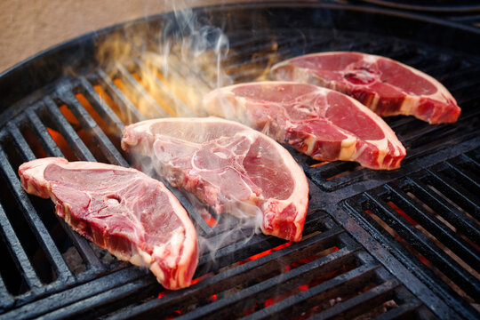 Rohe Lammr&uuml;ckensteaks gegrillt als close-up auf einem Holzkohlegrill mit Feuer