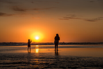 Silhouette of a woman and a child watching sunset from the beach. Sun over the horizon in the sea in summer