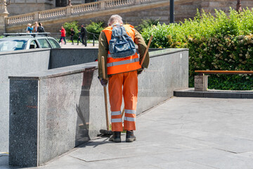 Municipal employee sweeping the city street, city janitor with a broom and dustpan in his hands and...