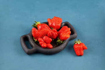 Fresh juicy berries in wooden serving plate. Unusual organic strawberries. Ugly fruits. Concept -...