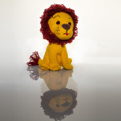 Amigurumi doll handmade yellow lion sitting - reflected on a light acrylic background.