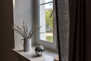 illow branches in a white ceramic jug and a mirrored disco ball on the windowsill as decoration before Easter