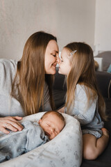 Portrait of mother with newborn son and infant daughter. Happy caucasian family of three people. Mother kiss her daughter. Selective focus. Film grain