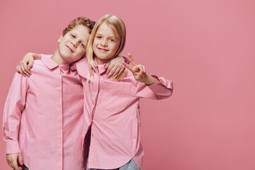 cute beautiful children stand in pink clothes on a pink background with their hands on each other's shoulders